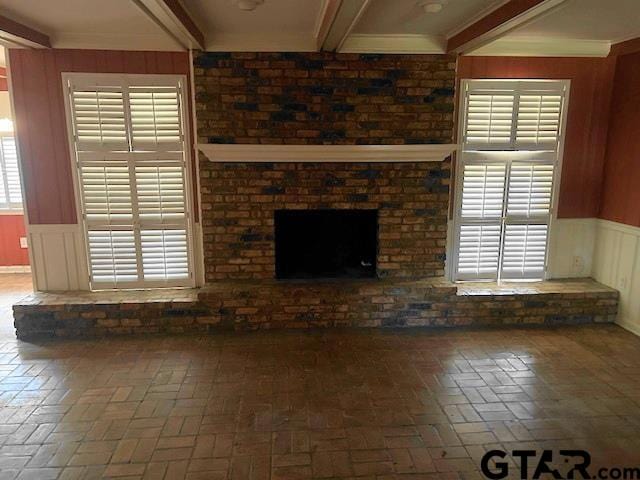 unfurnished living room featuring a wealth of natural light, a brick fireplace, crown molding, and beam ceiling