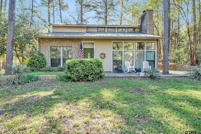 mid-century home featuring metal roof, a chimney, and a front yard