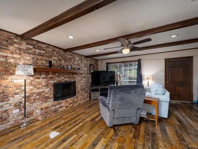 living area with a ceiling fan, a brick fireplace, beamed ceiling, and wood finished floors