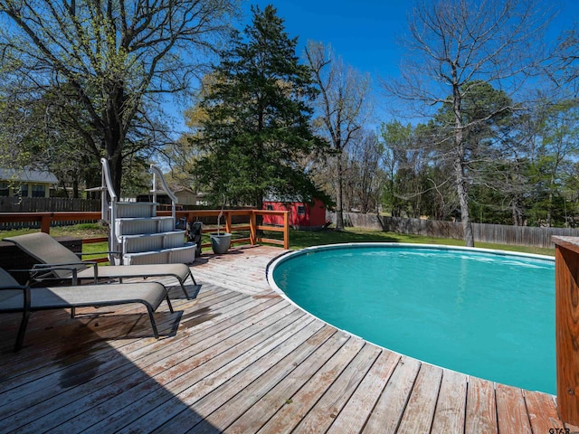 view of pool featuring an outdoor structure, a fenced backyard, a fenced in pool, and a wooden deck
