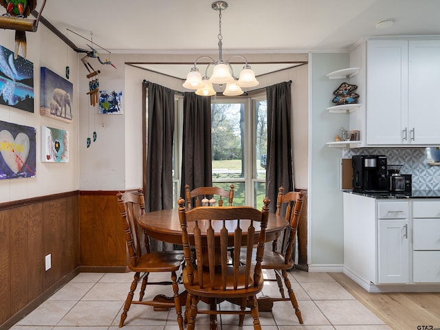 dining area featuring a notable chandelier, wood walls, light tile patterned floors, and wainscoting