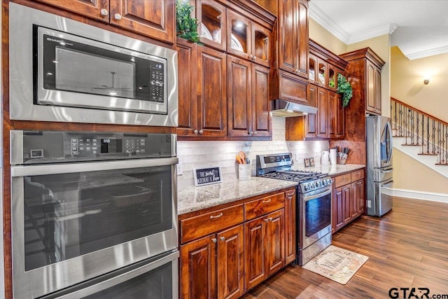 kitchen featuring stainless steel appliances, dark wood-type flooring, under cabinet range hood, crown molding, and tasteful backsplash