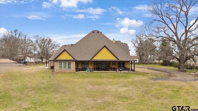 view of front of house featuring a front yard, roof with shingles, a chimney, a patio area, and brick siding