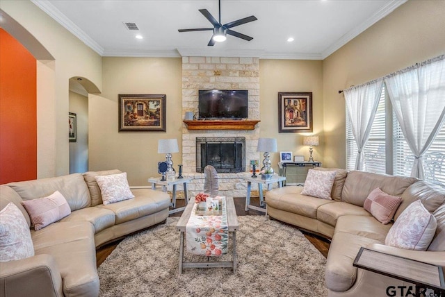 living area featuring visible vents, a stone fireplace, ornamental molding, and a ceiling fan