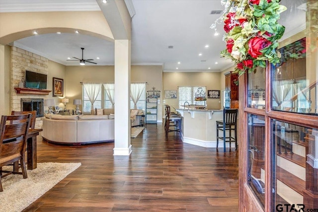 living area with baseboards, arched walkways, dark wood-style flooring, ceiling fan, and a stone fireplace