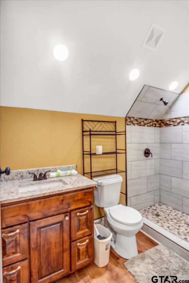 full bath with visible vents, toilet, vaulted ceiling, a tile shower, and wood finished floors