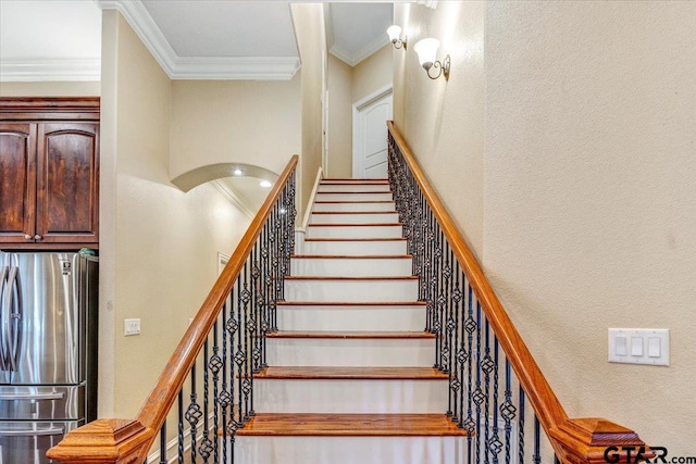 staircase with arched walkways, crown molding, and a textured wall