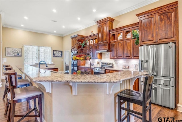 kitchen with a breakfast bar area, wood finished floors, visible vents, decorative backsplash, and appliances with stainless steel finishes