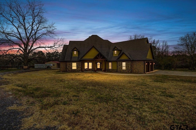 view of front facade featuring concrete driveway, a yard, and stone siding