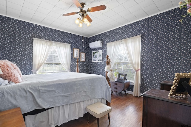 bedroom with wallpapered walls, wood finished floors, and a wall mounted air conditioner