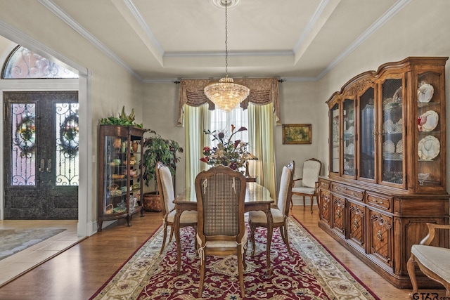 dining area featuring crown molding, a raised ceiling, a notable chandelier, and light wood-type flooring