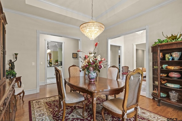 dining space featuring a chandelier, a raised ceiling, ornamental molding, and light hardwood / wood-style floors