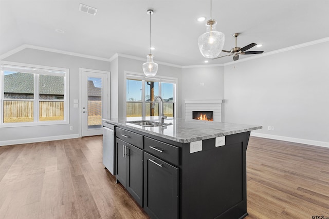 kitchen featuring decorative light fixtures, dishwasher, sink, a kitchen island with sink, and light stone counters