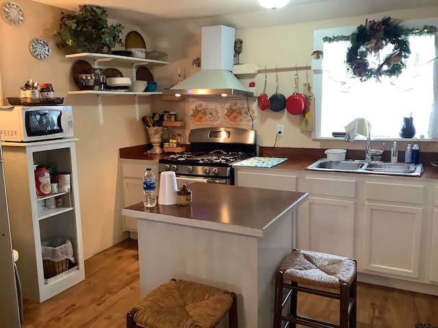 kitchen featuring island exhaust hood, sink, white cabinets, a breakfast bar area, and gas range