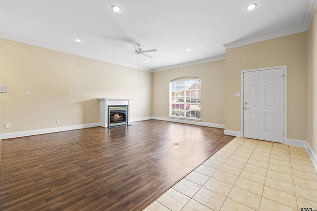 unfurnished living room with crown molding, a ceiling fan, wood finished floors, a lit fireplace, and baseboards