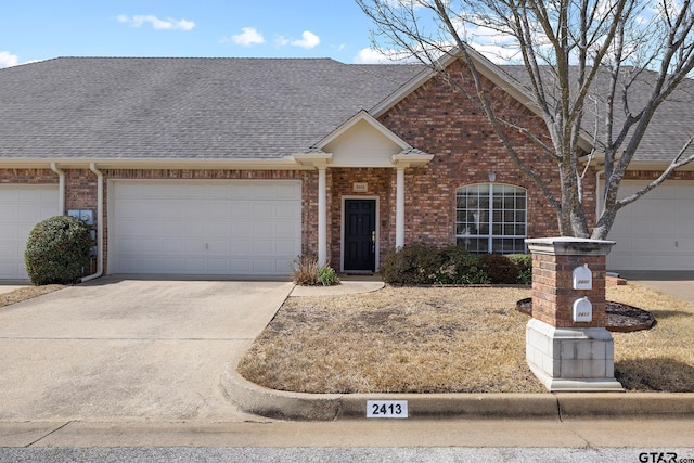 view of front of home with an attached garage, driveway, a shingled roof, and brick siding