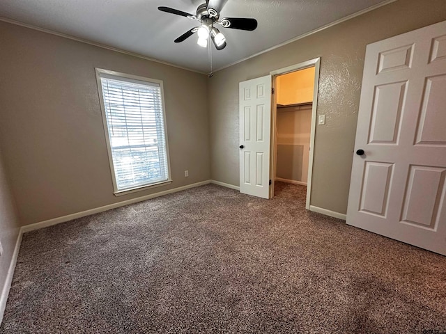 unfurnished bedroom featuring baseboards, carpet, a spacious closet, and crown molding