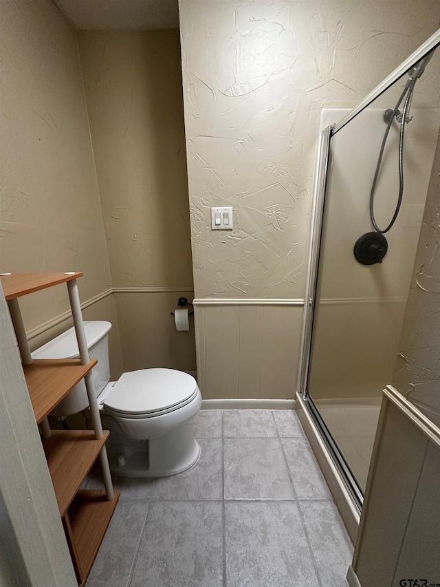 bathroom with a shower stall, toilet, a textured wall, and wainscoting