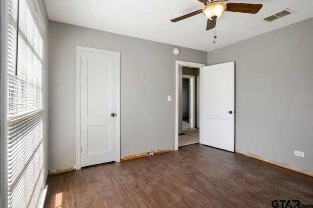 unfurnished bedroom with dark wood-style floors, a ceiling fan, visible vents, and baseboards