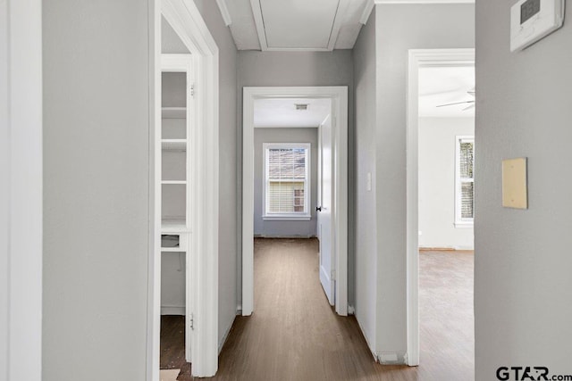 corridor with wood finished floors, attic access, and baseboards