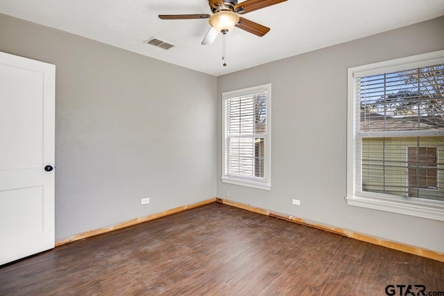 empty room with dark wood-type flooring, visible vents, baseboards, and a ceiling fan