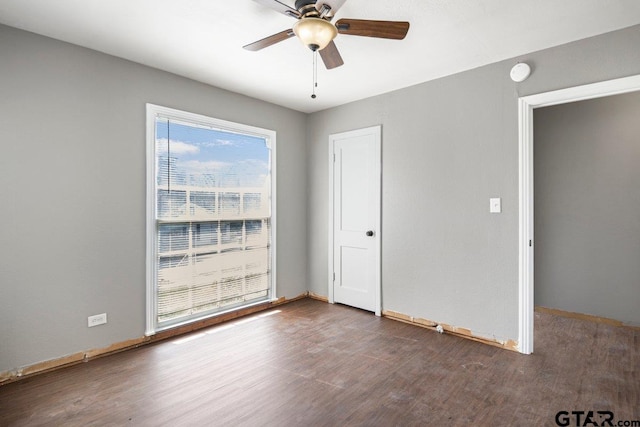 empty room featuring dark wood-type flooring, a ceiling fan, and baseboards