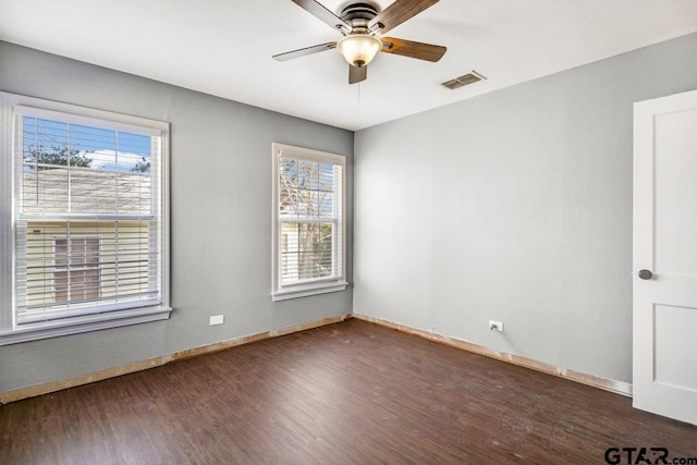 spare room featuring baseboards, ceiling fan, visible vents, and dark wood-style flooring