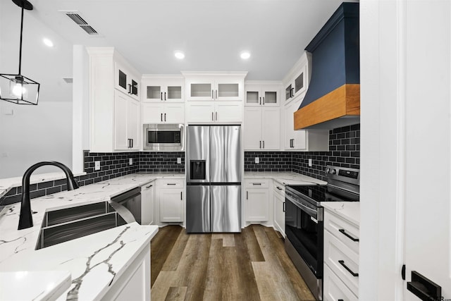 kitchen with appliances with stainless steel finishes, light stone counters, white cabinets, decorative light fixtures, and custom exhaust hood