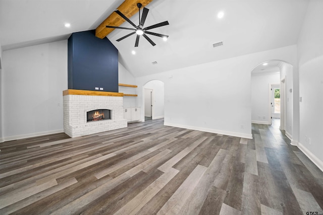 unfurnished living room with dark wood-type flooring, high vaulted ceiling, a brick fireplace, beamed ceiling, and ceiling fan