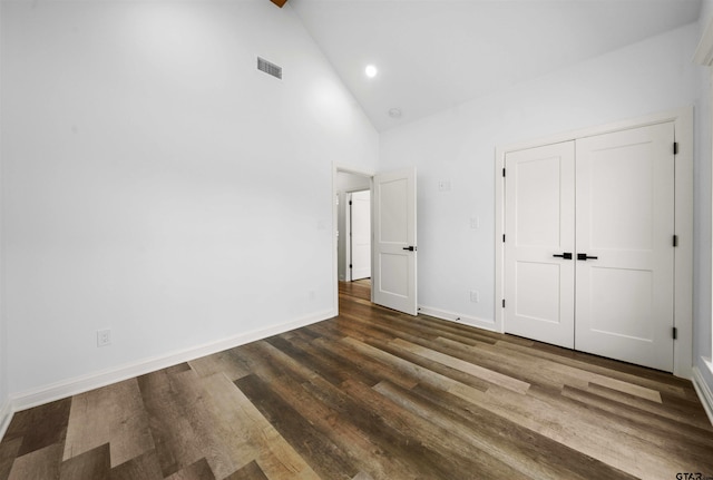 unfurnished bedroom with beamed ceiling, dark hardwood / wood-style flooring, high vaulted ceiling, and a closet