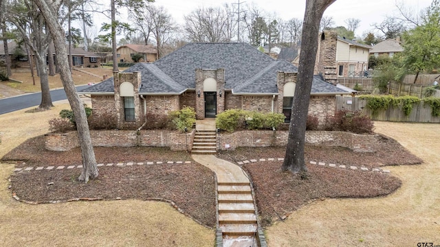 view of front of property featuring brick siding, fence, and roof with shingles