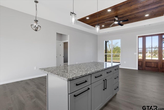 kitchen featuring a raised ceiling, ceiling fan, dark wood-type flooring, a center island, and hanging light fixtures