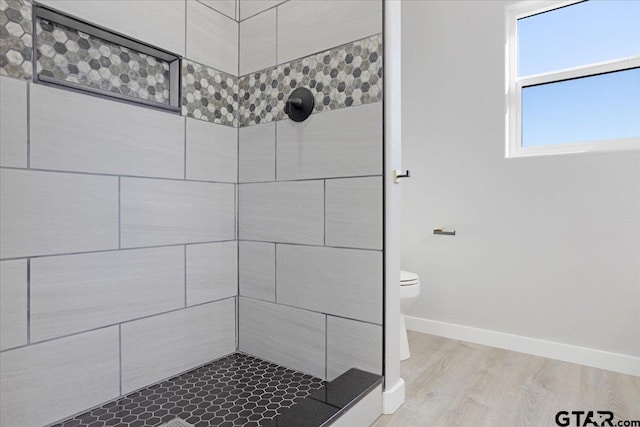 bathroom featuring hardwood / wood-style flooring, toilet, and a tile shower