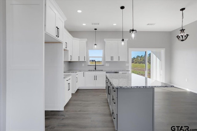 kitchen with white cabinets, a center island, light stone counters, and dark wood-type flooring