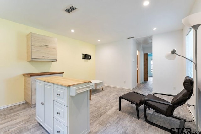 kitchen with a center island, white cabinetry, light brown cabinets, light wood-type flooring, and wooden counters