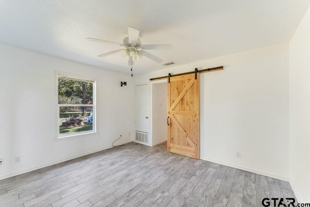 unfurnished bedroom featuring ceiling fan, light wood-type flooring, and a barn door