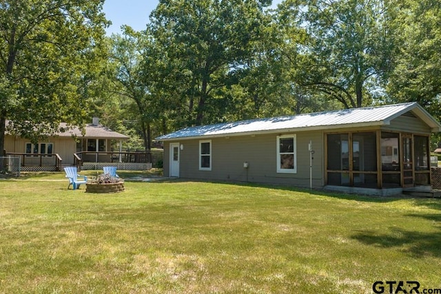 rear view of property featuring an outdoor fire pit, a deck, a lawn, and a sunroom