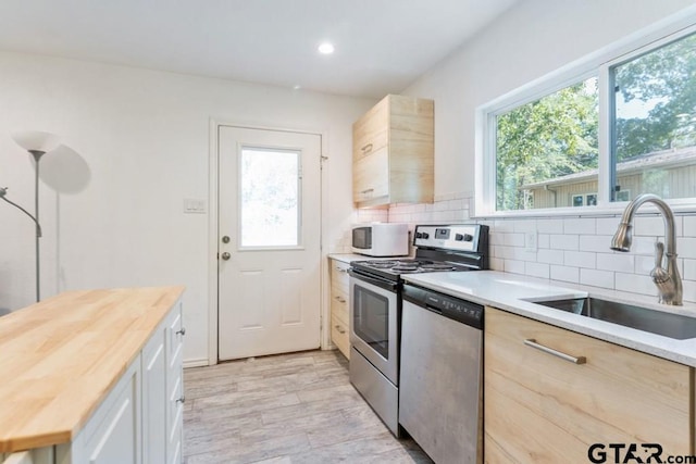 kitchen with wooden counters, stainless steel appliances, decorative backsplash, light brown cabinets, and sink