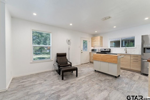 kitchen featuring appliances with stainless steel finishes, a center island, light brown cabinetry, and butcher block countertops