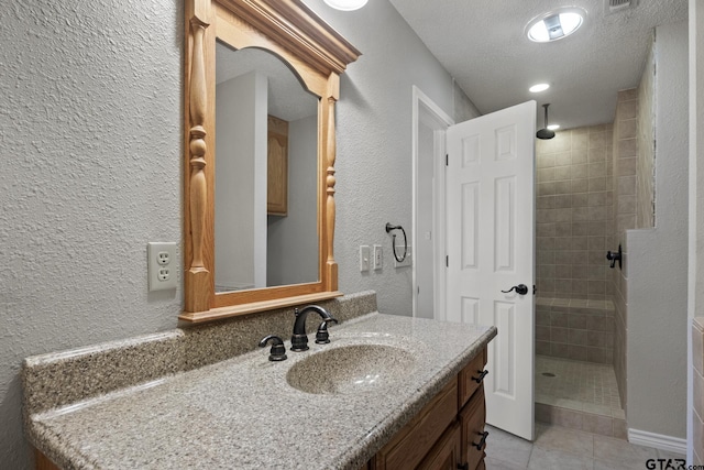 bathroom featuring tile patterned floors, vanity, a tile shower, and a textured ceiling