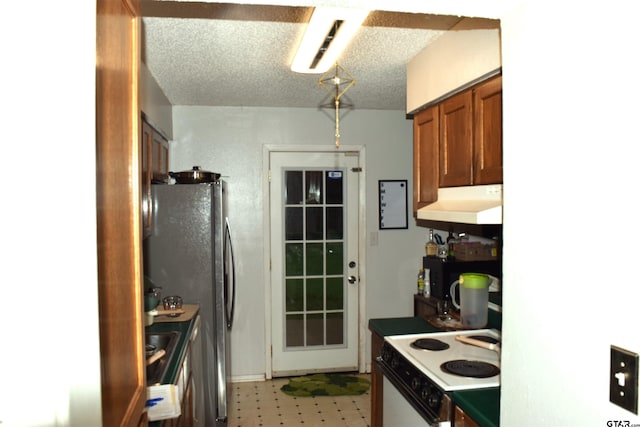 508 Baber St, Winnsboro, TX 75494 - kitchen with under cabinet range hood, white electric stove, freestanding refrigerator, brown cabinetry, and light flooring