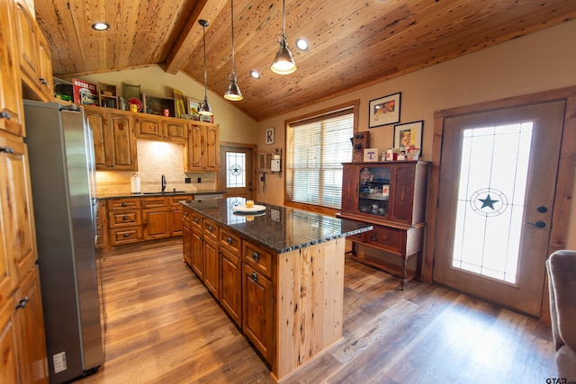 kitchen with sink, stainless steel fridge, dark stone countertops, hanging light fixtures, and a kitchen island