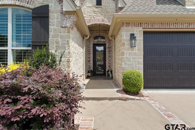 7417 Princedale, Tyler, TX 75703 - doorway to property with stone siding, a garage, a shingled roof, and concrete driveway