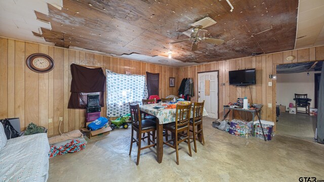 dining area featuring wood walls, concrete floors, and ceiling fan