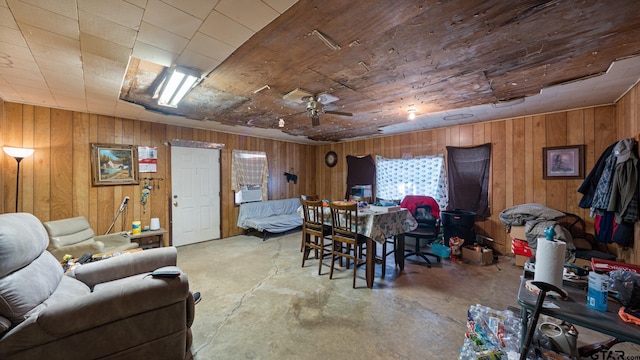 dining room with wood walls, ceiling fan, and concrete floors