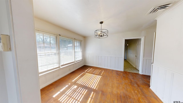 unfurnished room with wainscoting, visible vents, a notable chandelier, and wood finished floors