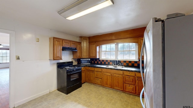 kitchen with under cabinet range hood, stainless steel appliances, a sink, decorative backsplash, and light floors