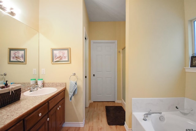 bathroom featuring wood finished floors, vanity, a bath, a stall shower, and baseboards