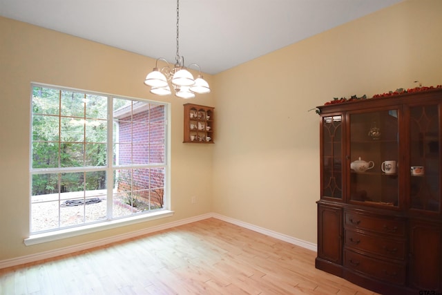 unfurnished dining area featuring a chandelier, plenty of natural light, light wood-type flooring, and baseboards