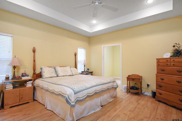 bedroom with light wood-style floors, a tray ceiling, recessed lighting, and a ceiling fan